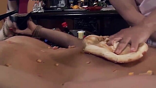 In this image, a tied girl is humiliated with food in a dirty and messy role play, involving a female sex slave and BDSM elements.